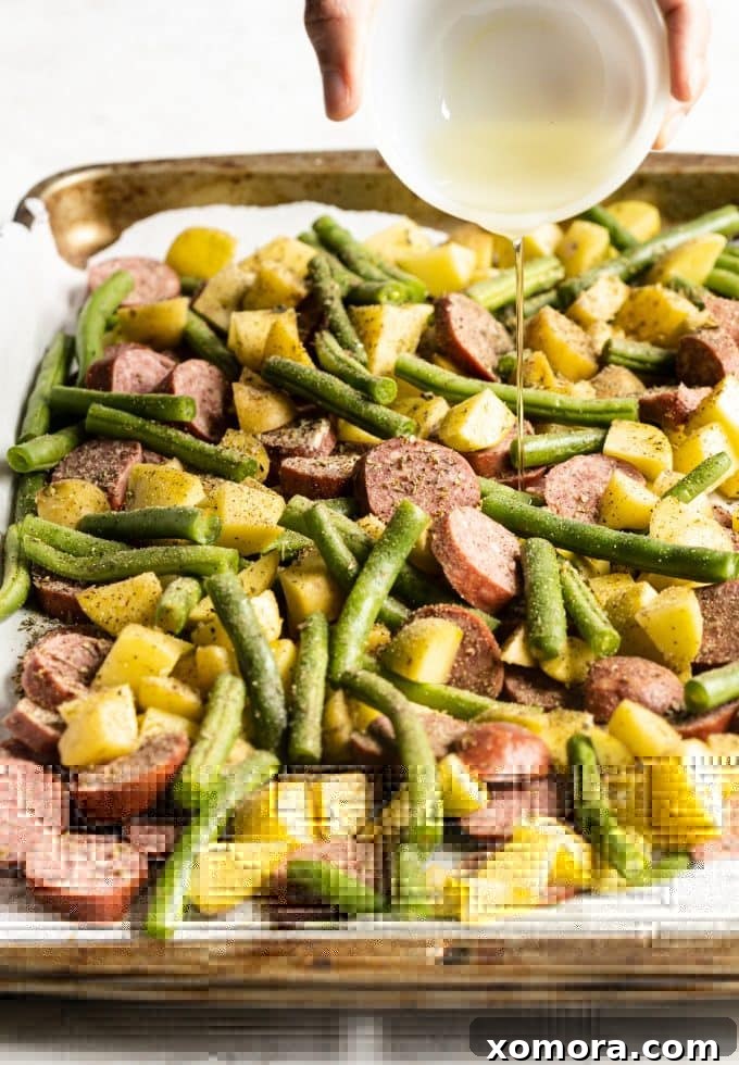 Sheet Pan Sausage and Roasted Vegetables 3 Sliced fully cooked sausage, chopped potatoes, and fresh green beans tossed with olive oil and seasonings on a baking sheet, ready for roasting.