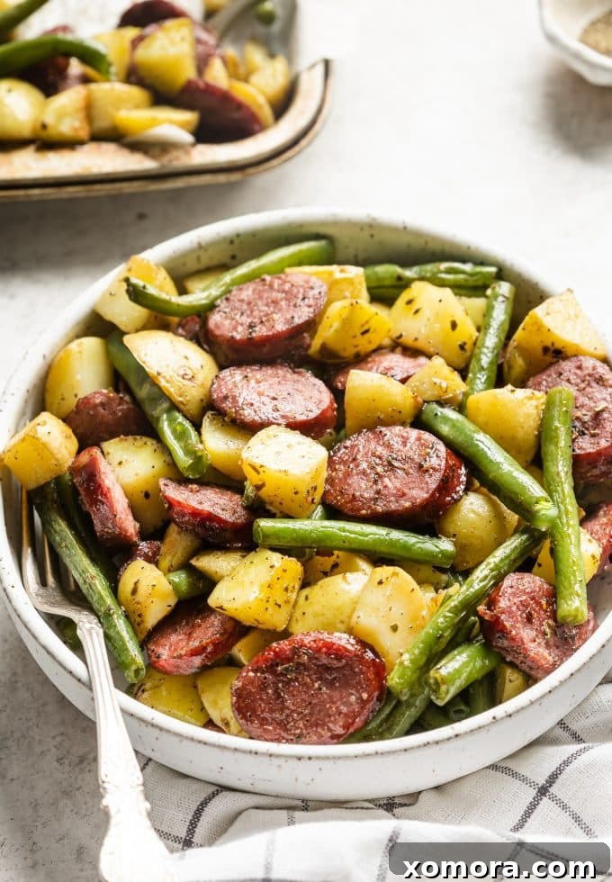 Sheet Pan Sausage and Roasted Vegetables 5 A serving of roasted sheet pan sausage, potatoes, and green beans on a white plate, garnished with fresh herbs.
