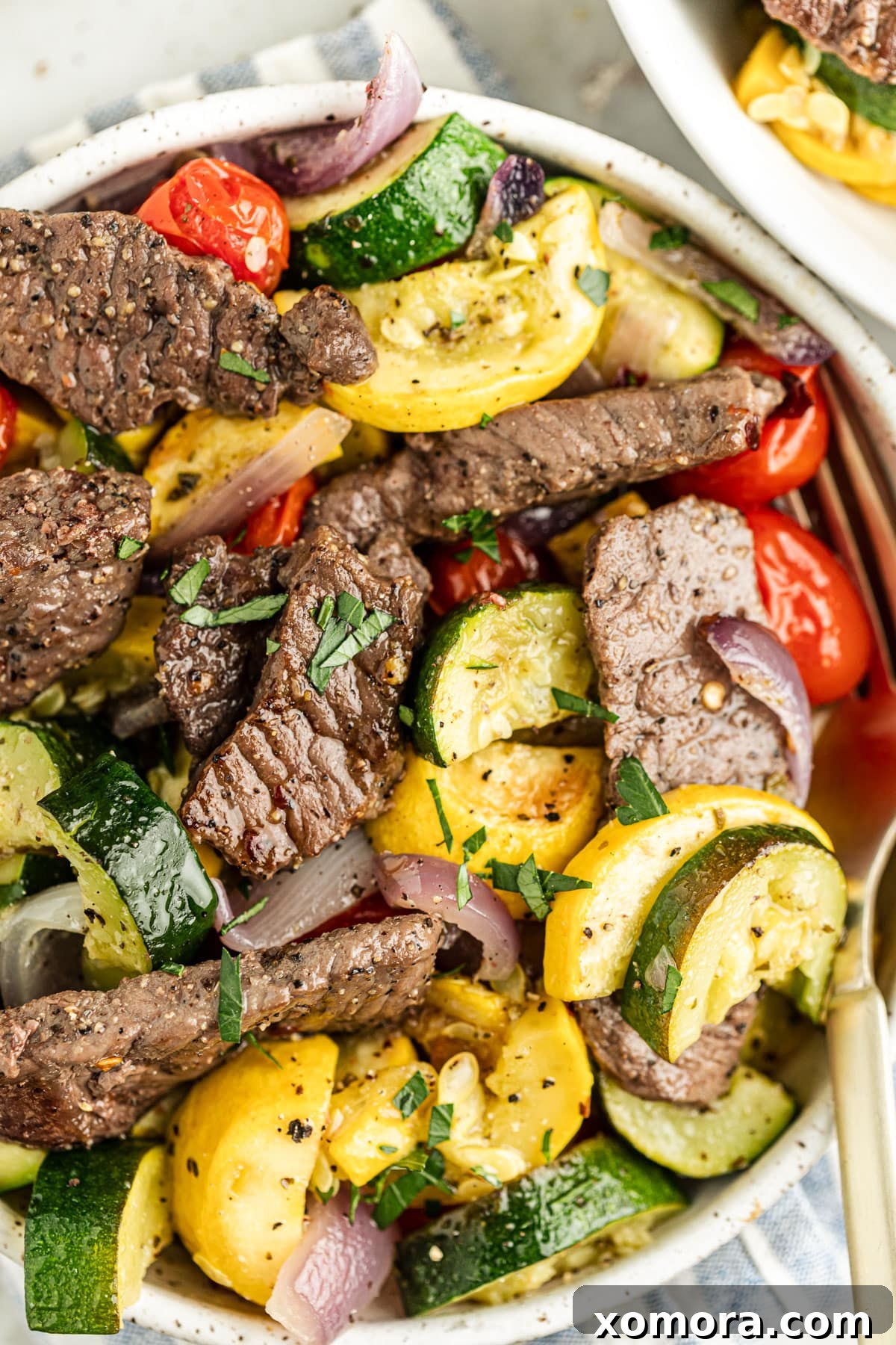 Close-up of perfectly roasted sirloin steak slices with colorful zucchini, yellow squash, cherry tomatoes, and red onion on a sheet pan, ready to serve.