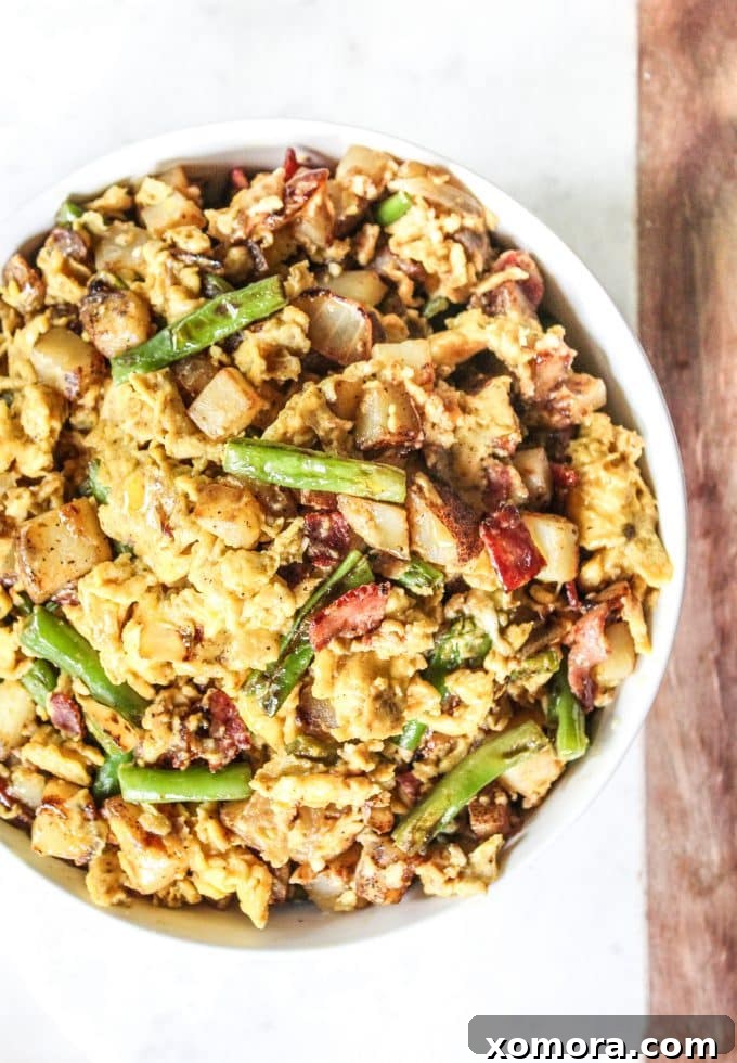 Brunch Bliss Scramble 2 A vibrant, close-up shot of a breakfast scramble with fluffy eggs, crispy bacon bits, golden-brown potatoes, and bright green beans, all mixed together in a skillet, ready to be served.