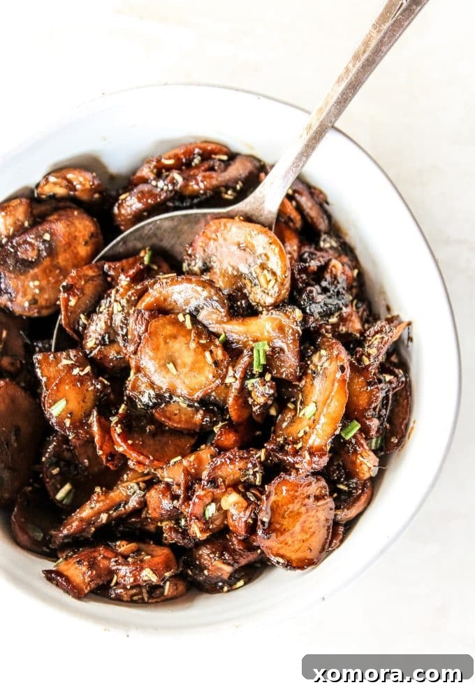 A close-up of sautéed garlic mushrooms in a skillet, showing the browning process and bubbling butter and sauce.