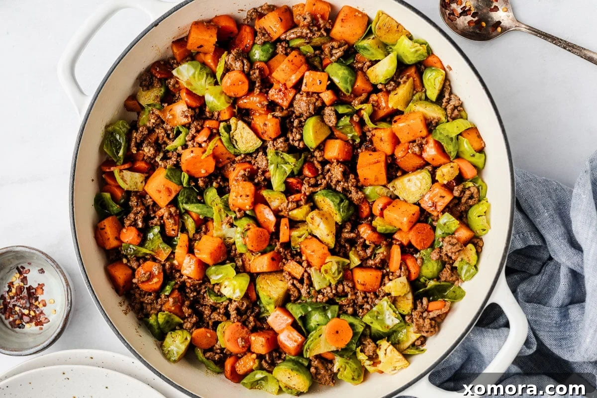 Savory Beef and Sweet Potato Hash 6 A serving of ground beef and sweet potato skillet in a white bowl, ready to eat, with a fork digging in.
