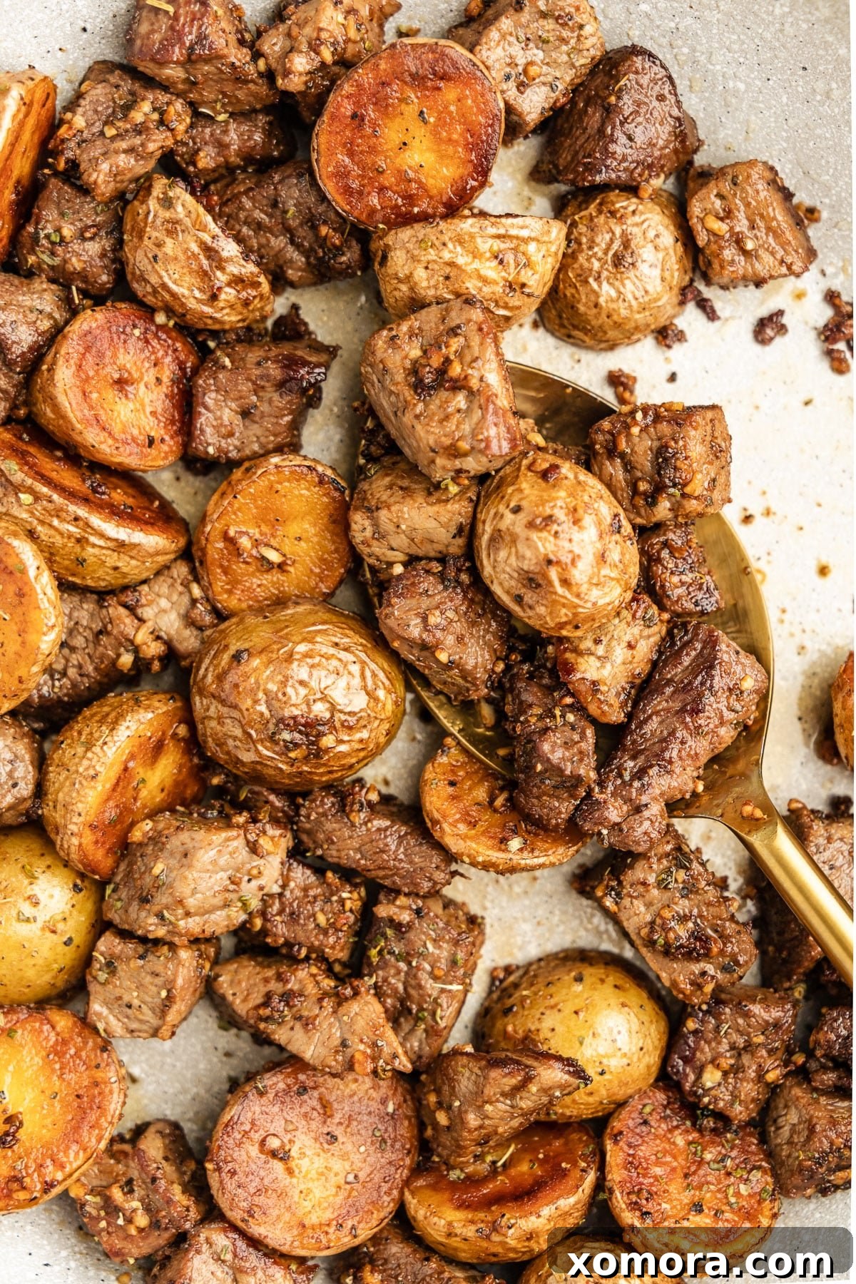 Sizzling Garlic Steak & Cris Crispy Potatoes 2 Close-up of a sizzling skillet filled with perfectly cooked garlic steak bites and golden brown potatoes, garnished with fresh herbs.