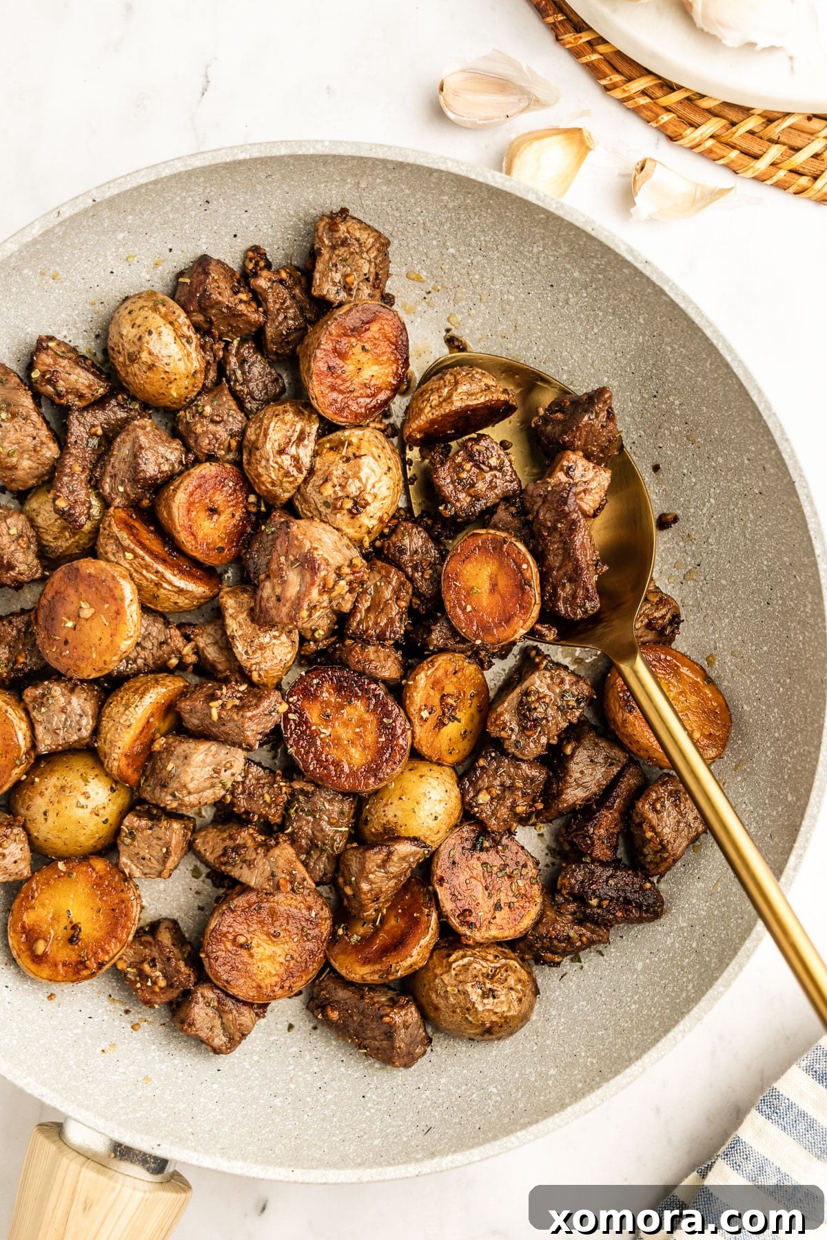 Sizzling Garlic Steak & Cris Crispy Potatoes 3 A top-down view of garlic steak and potatoes in a large skillet, showing the golden potatoes and seared steak pieces.