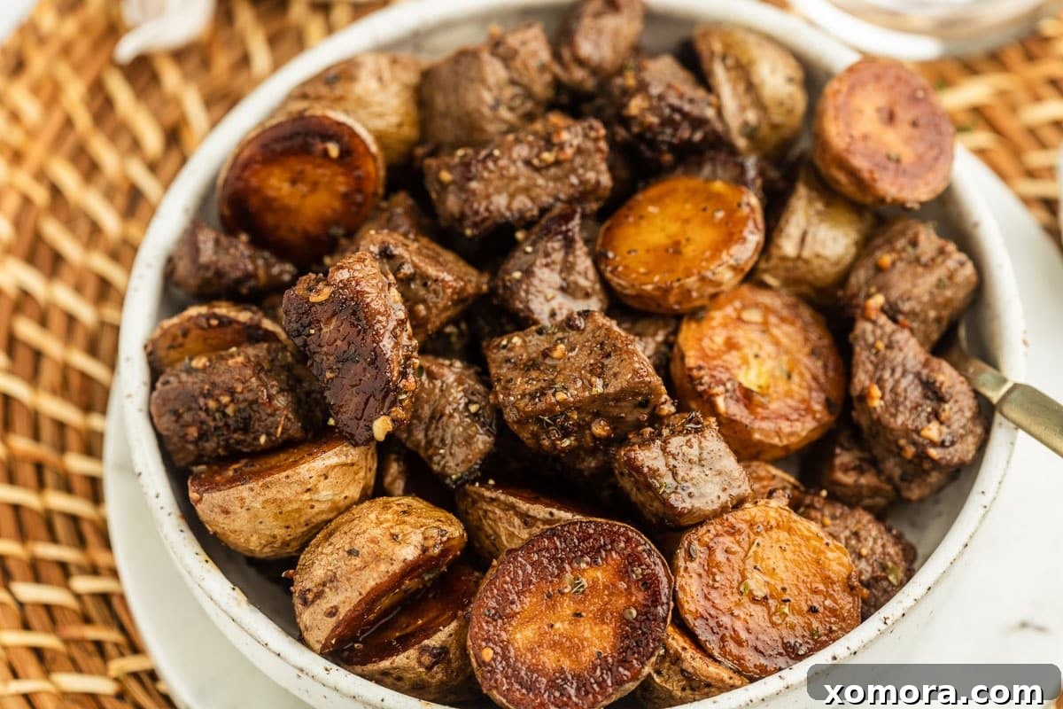 Sizzling Garlic Steak & Cris Crispy Potatoes 4 A close-up of a hand seasoning sirloin steak bites in a skillet next to already browned baby Dutch yellow potatoes.