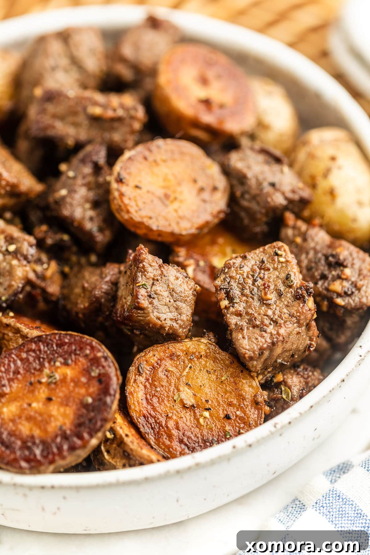 Sizzling Garlic Steak & Cris Crispy Potatoes 5 A close-up of a serving of skillet garlic steak and potatoes in a white bowl, garnished with fresh herbs, ready to be enjoyed.
