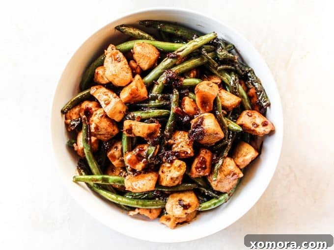 Chicken pieces browning in a hot skillet with green beans nearby