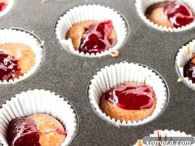 Layered almond butter and jelly cups in a muffin pan, showing the chocolate, nut butter, and jelly layers before final chocolate topping.