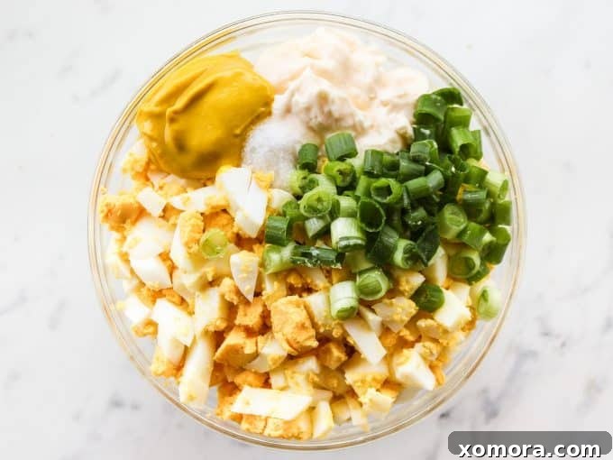 Close-up shot of creamy classic egg salad with visible chopped eggs and green onions, served in a white bowl.