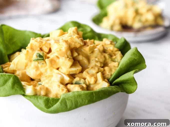 A close-up of the finished classic egg salad, with chopped eggs, mayonnaise, and green onions visible, scooped onto a small serving plate.