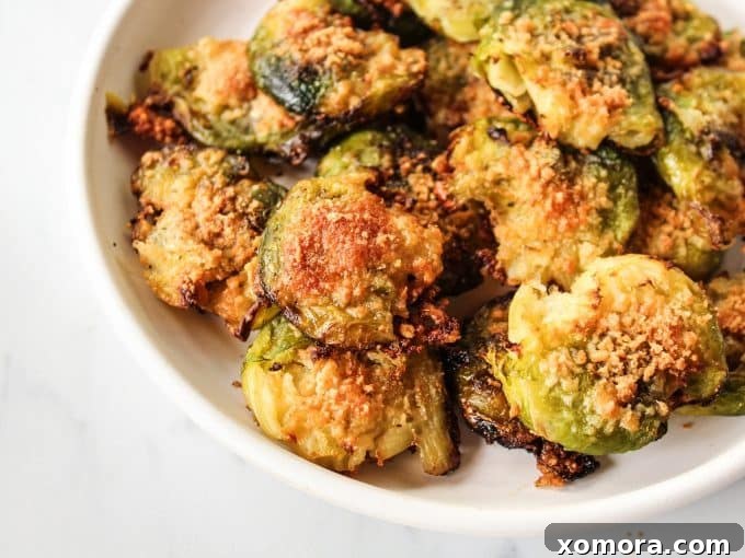 Crispy Parmesan Smashed Brussels Sprouts 5 A hand gently smashing a boiled brussels sprout on a baking sheet with a potato masher.