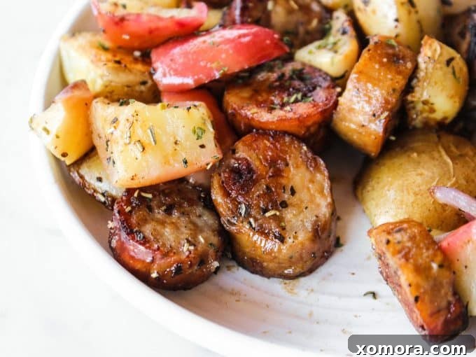 Ingredients for sheet pan sausage, apples, and potatoes neatly arranged on a cutting board, including sliced sausage, red onion, apples, and potatoes.