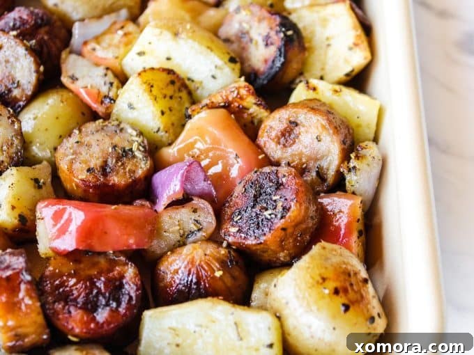 Sausage, apple, potato, and red onion pieces, beautifully seasoned and spread in a single layer on a baking sheet, ready for the oven.