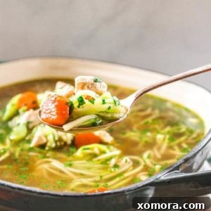 Close-up of a serving of Chicken Zoodle Soup, highlighting the chicken, zucchini noodles, and rich broth.