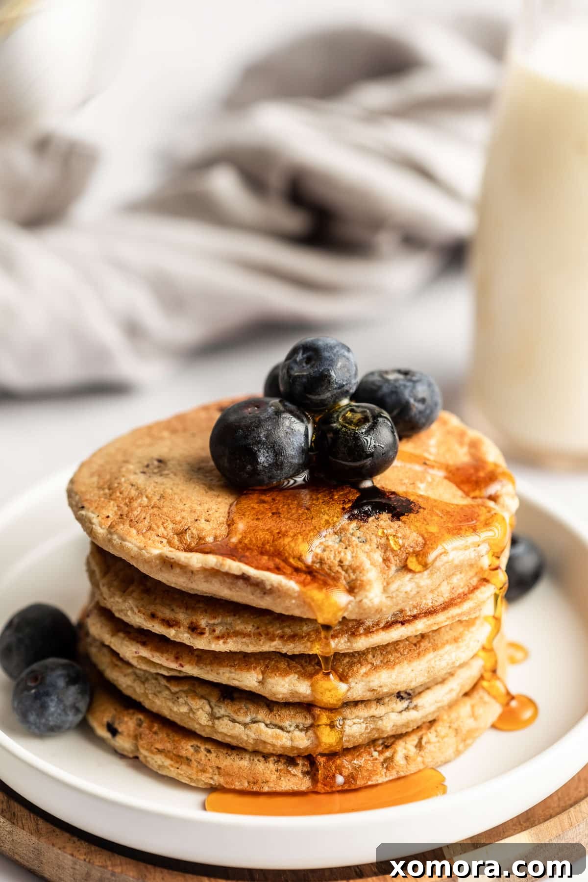 Blueberry Oat Power Pancakes 2 A stack of fluffy blueberry oat pancakes drizzled with maple syrup, with fresh blueberries on top.