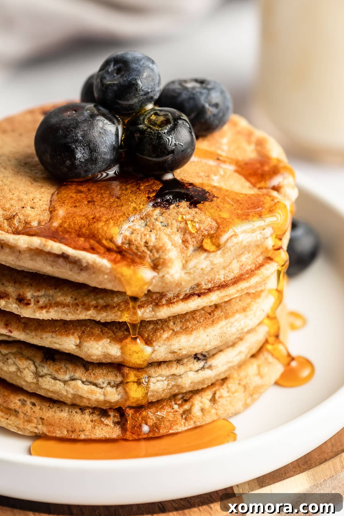 Blueberry Oat Power Pancakes 4 Three healthy blueberry oat pancakes stacked on a white plate, garnished with fresh blueberries.