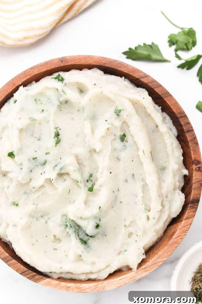 Velvety Cauliflower Mash 2 Creamy cauliflower mashed potatoes served in a white bowl with a sprig of rosemary.