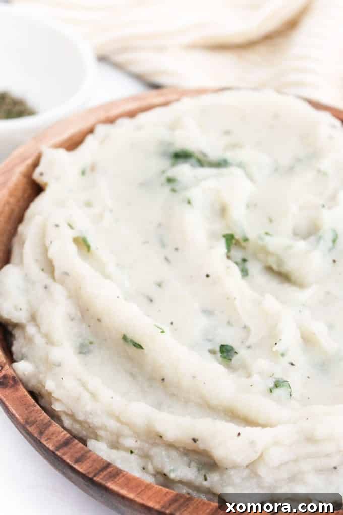 Velvety Cauliflower Mash 4 A close-up shot of fluffy and creamy cauliflower mashed potatoes in a white bowl, ready to be served.