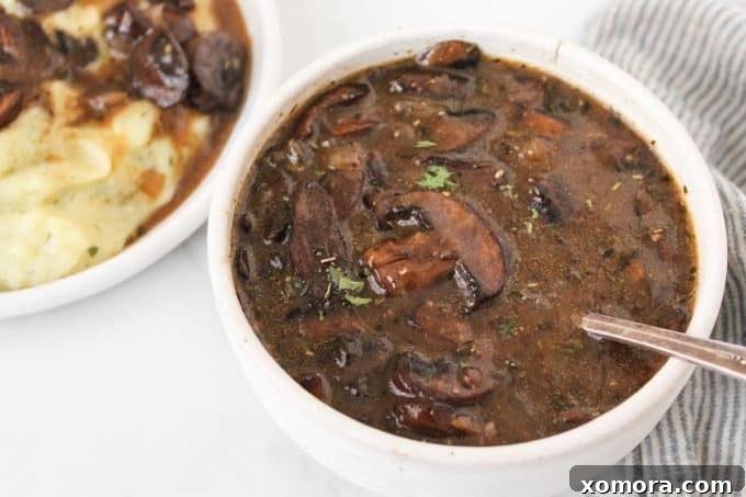Effortless Umami Mushroom Gravy 4 A serving spoon lifting a generous amount of thick mushroom gravy from a bowl, highlighting its rich consistency.