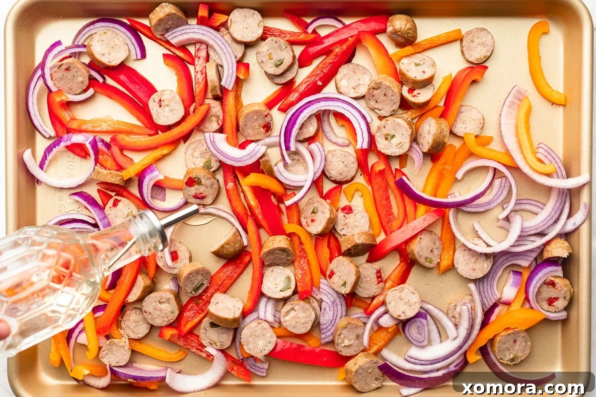 Effortless Roasted Italian Sausage and Peppers 3 Close-up of chopped sausage, bell peppers, and onions tossed with seasonings on a sheet pan.