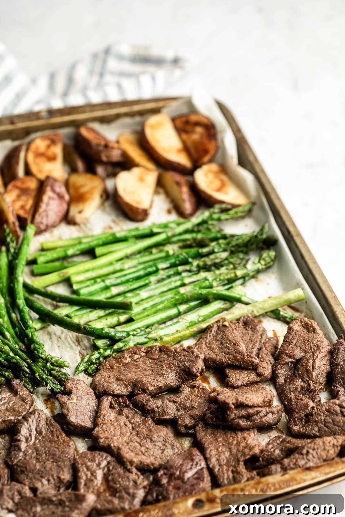 Sheet Pan Steakhouse at Home 2 Close-up of a perfectly cooked sheet pan steak dinner with steak, asparagus, and potato wedges.