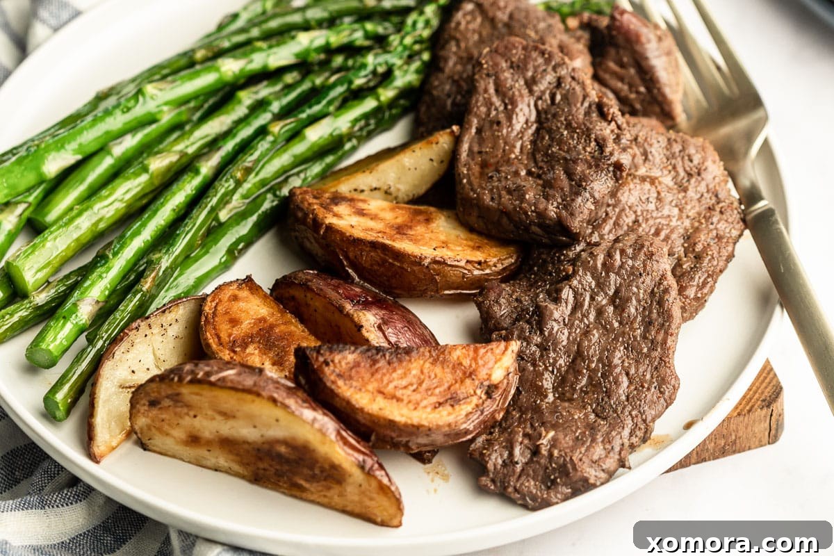 Sheet Pan Steakhouse at Home 3 Ingredients for a sheet pan steak dinner laid out on a cutting board, including sliced sirloin steak, potatoes, and asparagus.