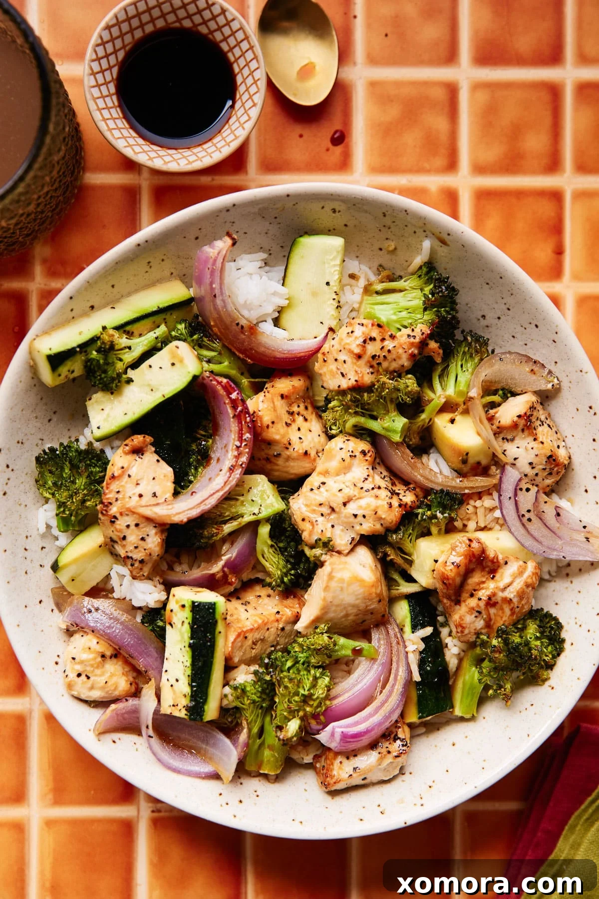 Sheet Pan Roasted Chicken and Seasonal Vegetables 2 Close-up of baked chicken and vegetables on a sheet pan, showcasing marinated chicken pieces, bright green broccoli, sliced zucchini, and red onion.