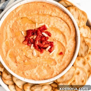 Creamy Roasted Red Pepper Hummus garnished with olive oil and spices in a white bowl.