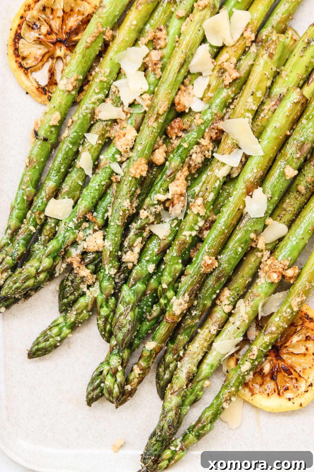Golden Parmesan Asparagus 2 A close-up of beautifully sautéed asparagus spears with parmesan cheese and lemon wedges on a rustic white plate, ready to serve.