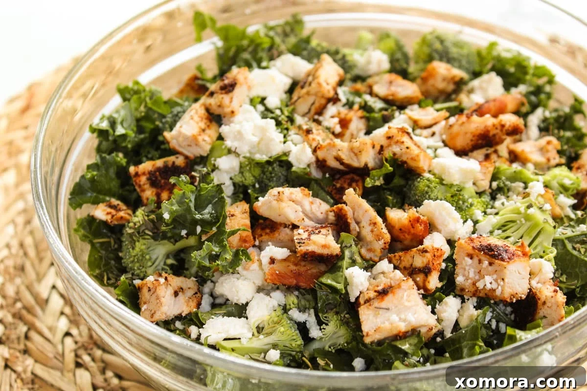 Hearty Chicken & Kale Salad 3 Close-up of the dressing being poured over the chopped kale and broccoli in a glass mixing bowl.
