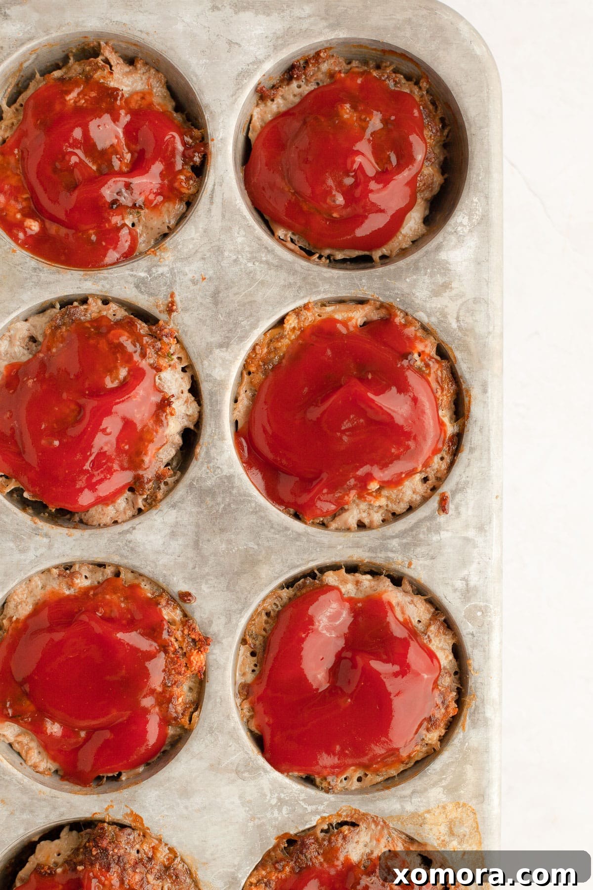 Savory Meatloaf Cups 5 A baked meatloaf muffin being removed from a muffin tin, showing its perfectly browned exterior.