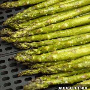 Close-up of golden-brown air fryer asparagus in a white bowl, garnished with lemon.