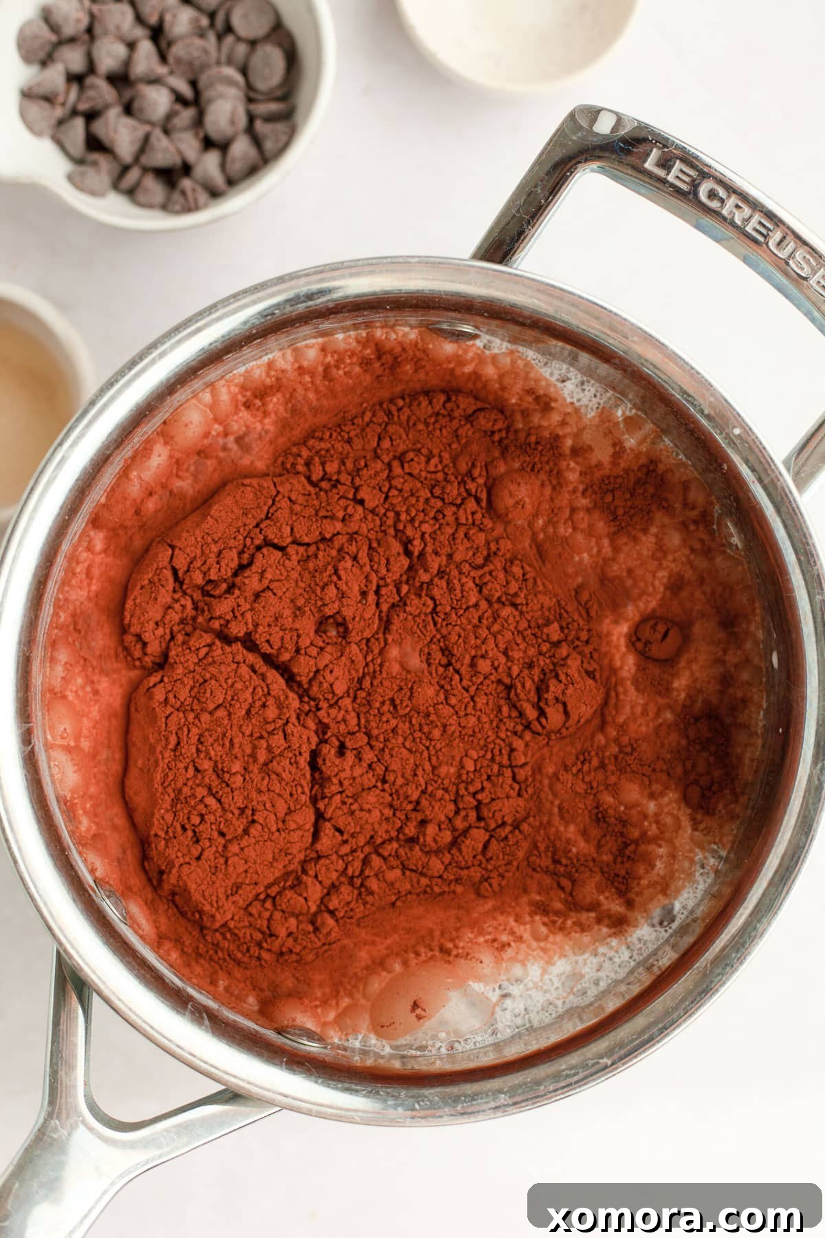 Wholesome Peppermint Hot Cocoa 3 A close-up of a pot on the stove, showing milk, cocoa powder, and maple syrup being whisked together for homemade hot chocolate.