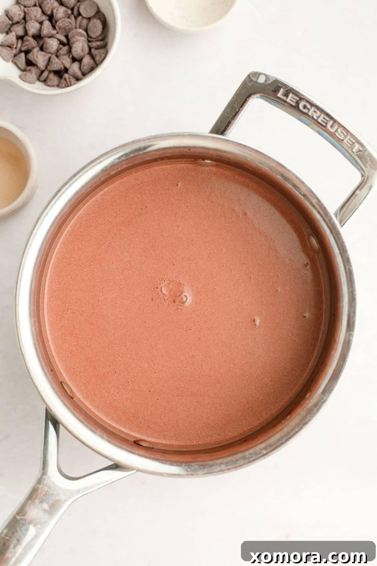 Wholesome Peppermint Hot Cocoa 4 A stainless steel pot with homemade hot chocolate simmering gently on a stovetop, with a whisk stirring the mixture.