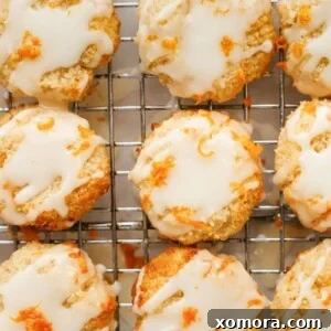 Zesty Orange Almond Delights 7 Close-up of a single orange almond cookie with glaze and zest on a white plate.