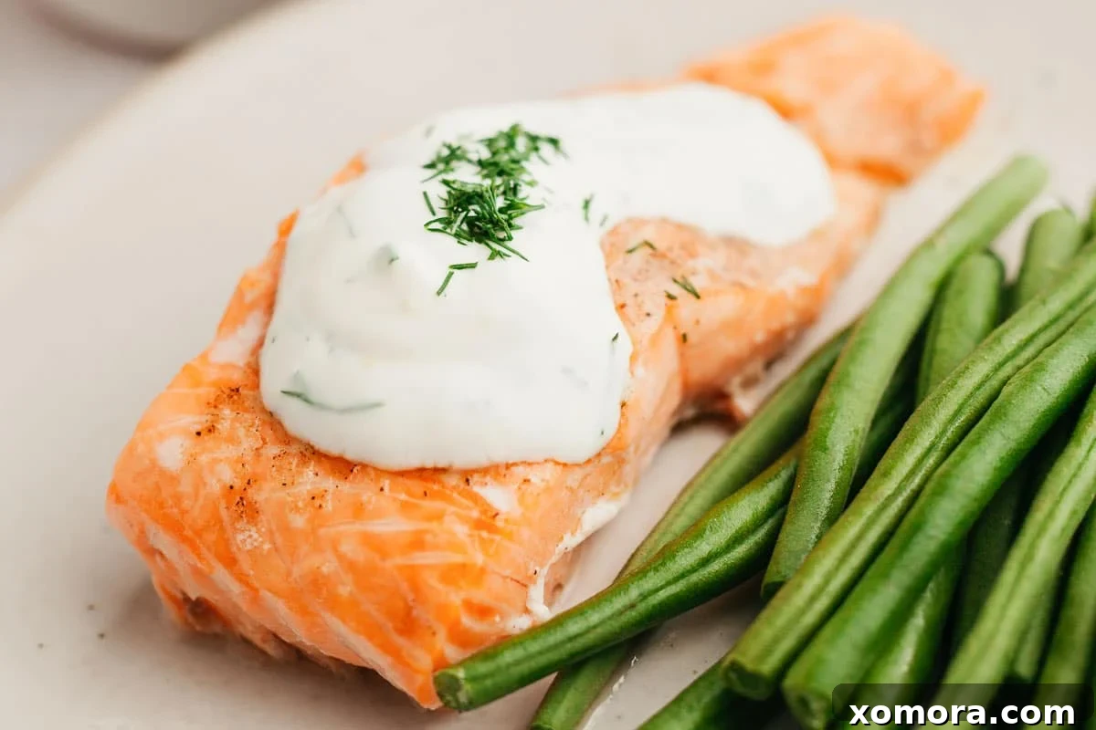Deliciously Simple Lemon Dill Oven Salmon 7 Full plate of oven-baked salmon with lemon dill sauce and a side of green vegetables.
