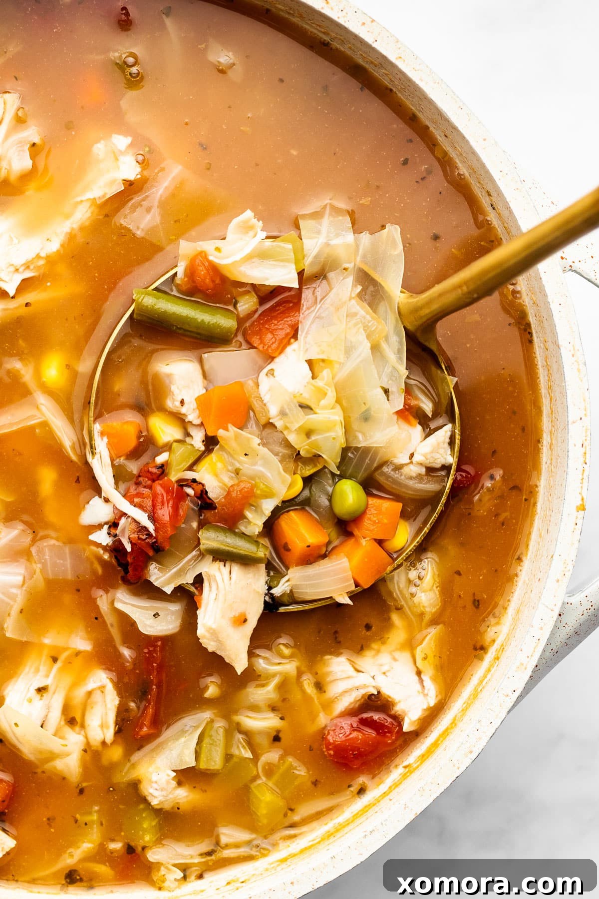 A close-up shot of a single serving of chicken vegetable soup in a bowl, with a spoon ready.