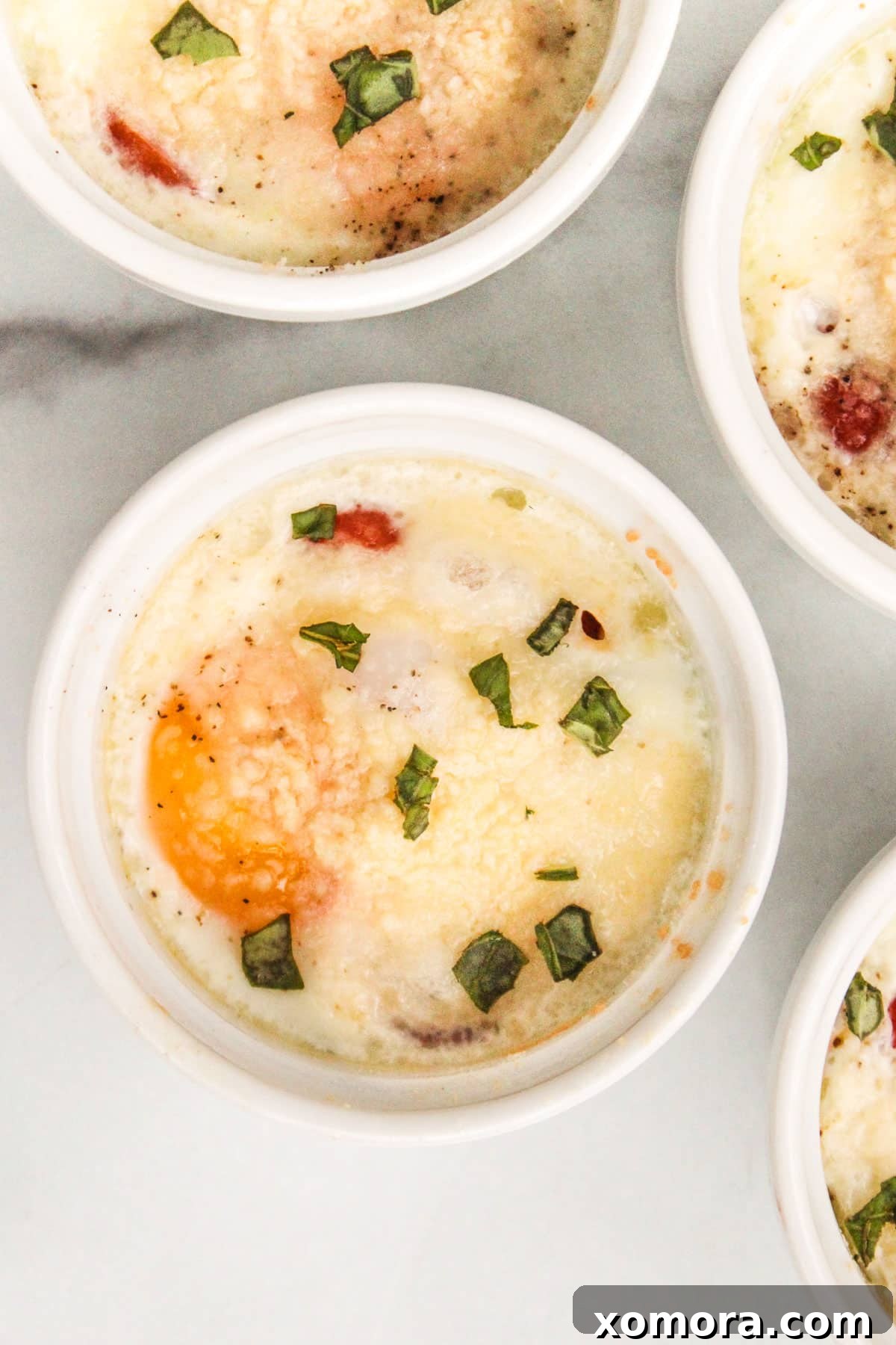 A close-up of a single baked egg in a ramekin, perfectly cooked with melted parmesan cheese and fresh basil garnish.