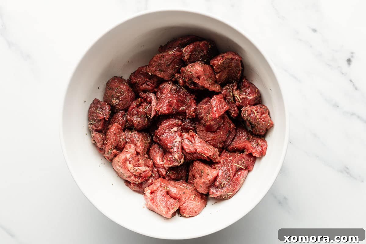 Air fryer steak bites mixed with Italian seasoning, garlic powder, salt, and pepper in a bowl.