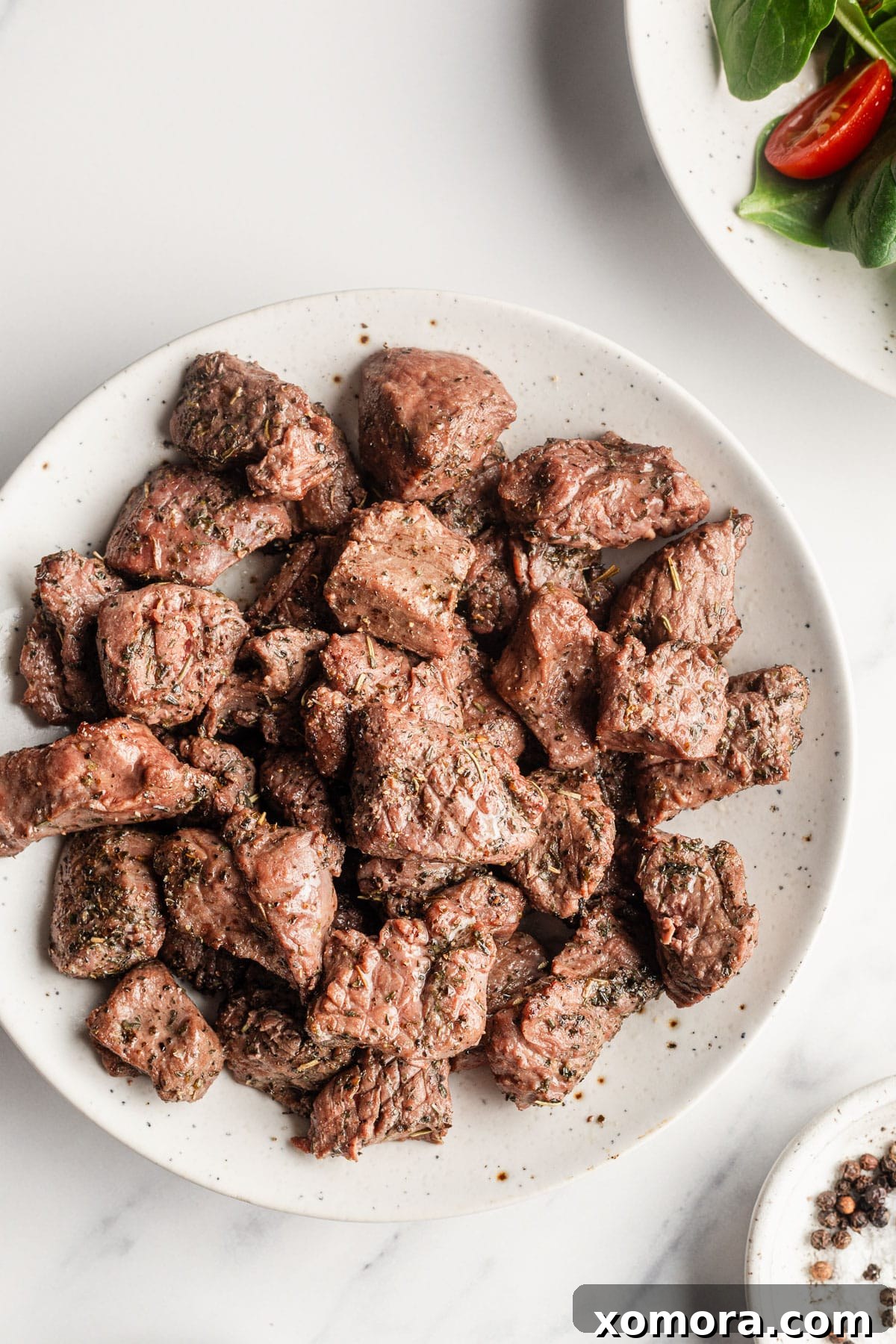 Air fryer steak bites served with a side of sauce and fresh herbs.