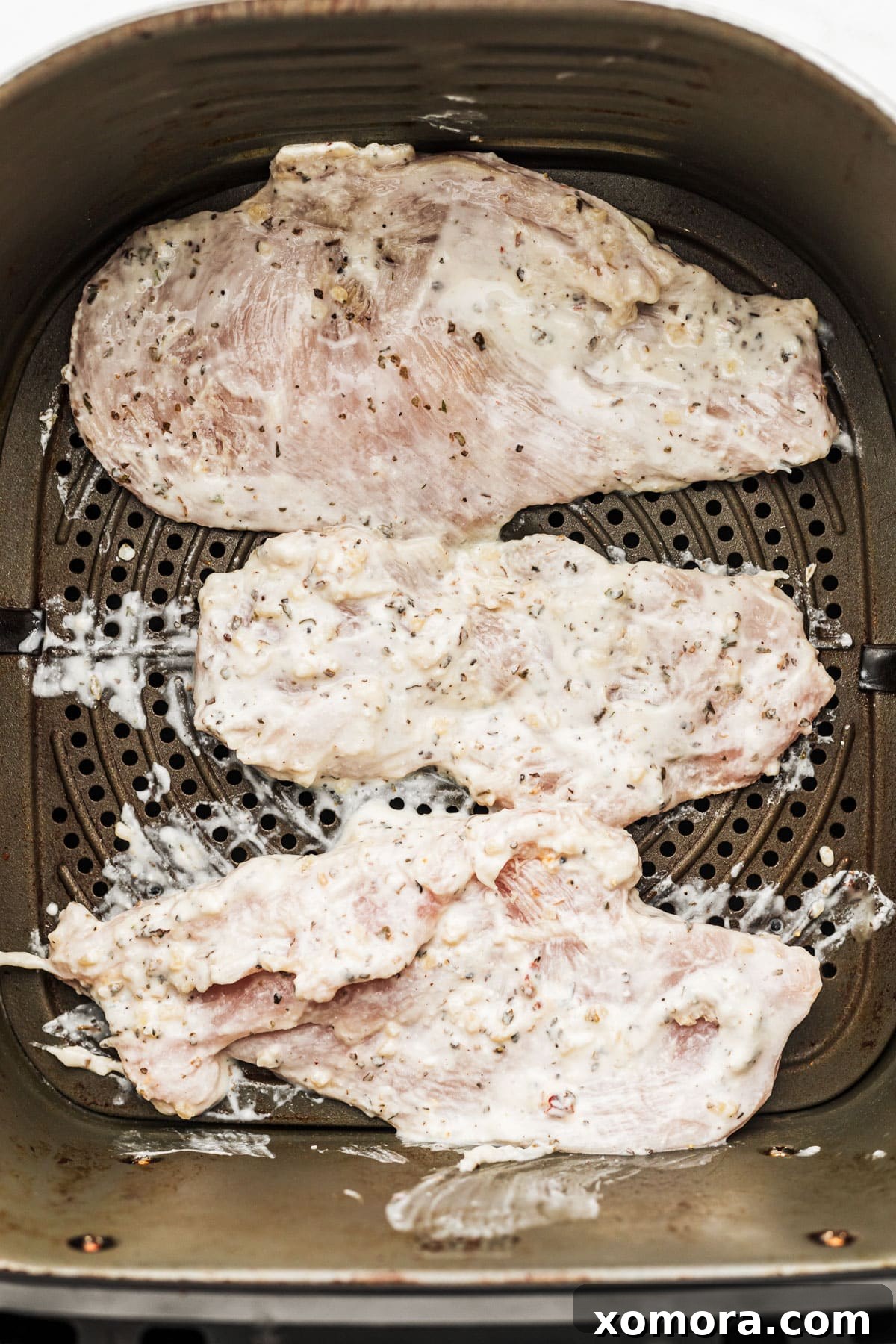 Golden Air Fryer Yogurt Chicken 4 Prepared chicken breasts coated in yogurt marinade in a bowl.