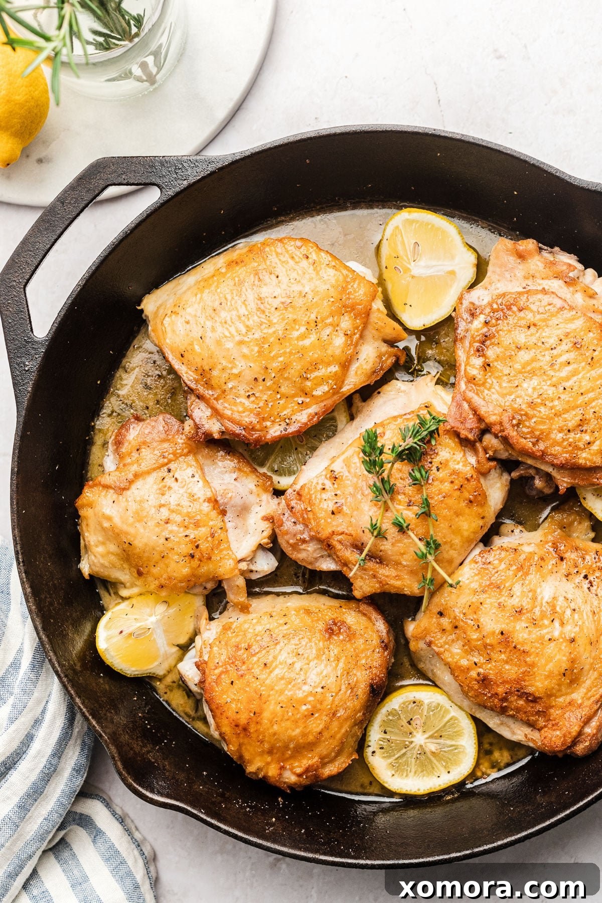 Zesty Lemon Roasted Chicken Thighs 2 Crispy, golden-brown baked lemon herb chicken thighs garnished with fresh lemon slices and aromatic herbs, presented in a cast iron skillet.