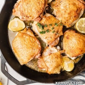 A close-up of a perfectly cooked, juicy baked lemon herb chicken thigh, beautifully garnished with fresh herbs and lemon slices.
