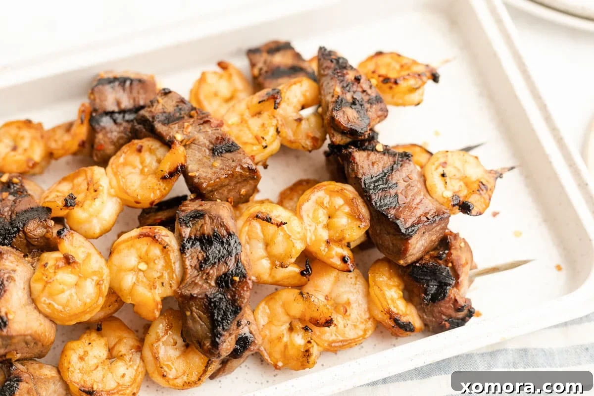 Surf and Turf Skewers 4 Three grilled steak and shrimp kabobs resting on a cutting board with fresh herbs.