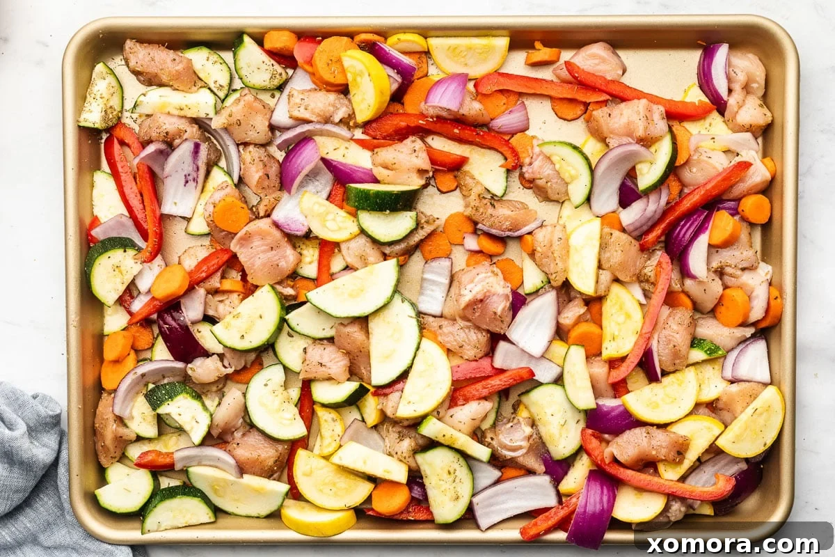 Close-up of roasted chicken and vegetables on a sheet pan, showing colorful array.