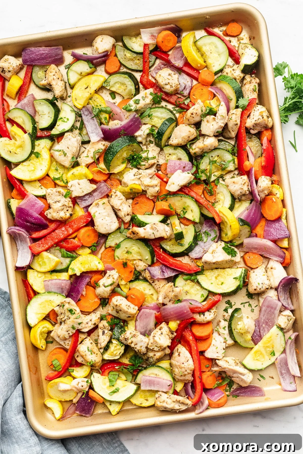 A large sheet pan with roasted chicken, zucchini, yellow squash, carrots, bell pepper, and red onion. Finished dish.