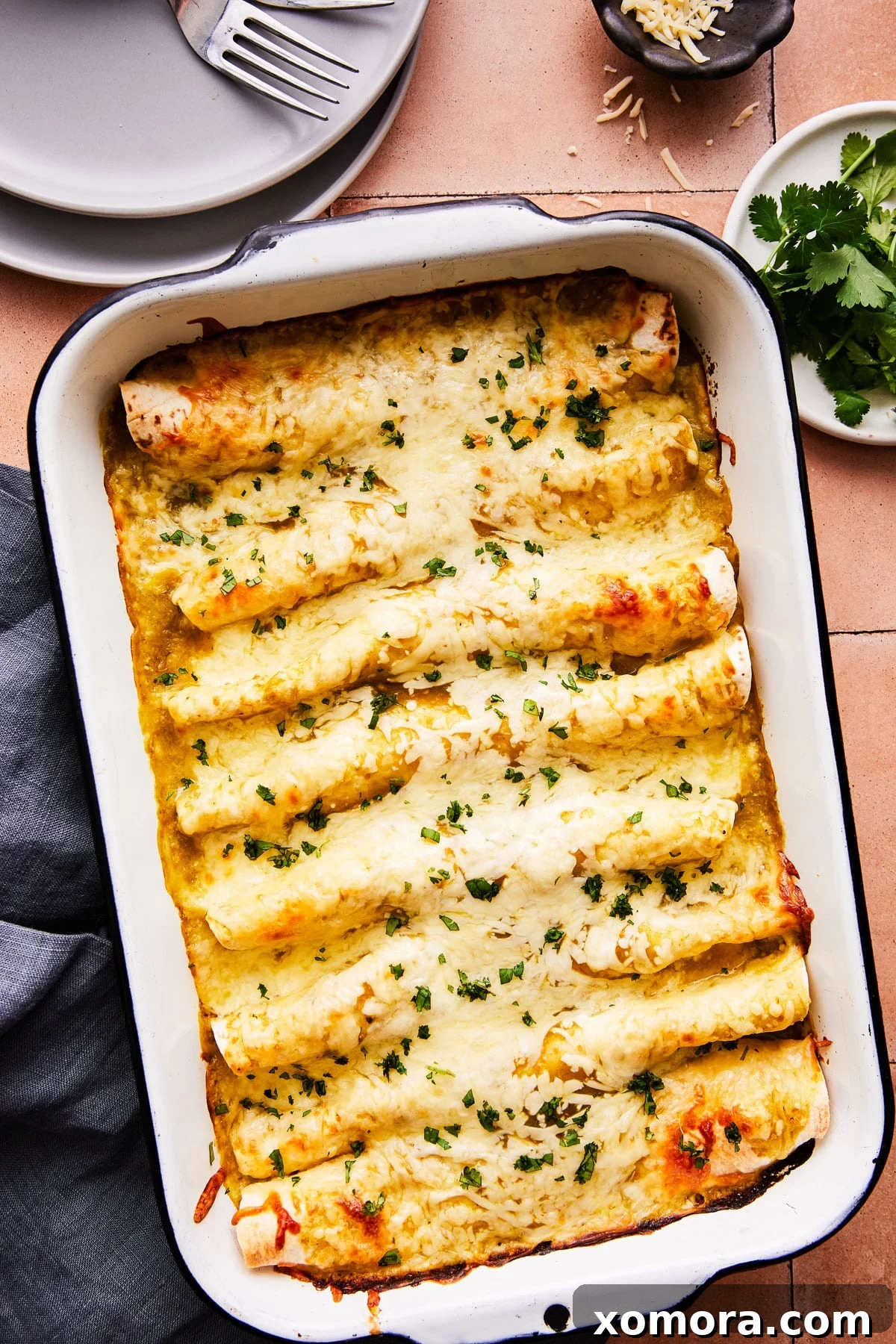 Effortless Green Chile Chicken Enchiladas 2 Close-up of a baking dish filled with vibrant green salsa verde chicken enchiladas, topped with melted cheese and fresh cilantro.