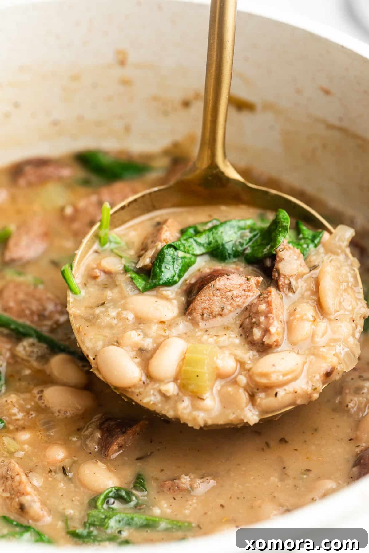 A bowl of creamy sausage and white bean soup garnished with fresh herbs and pepper flakes.