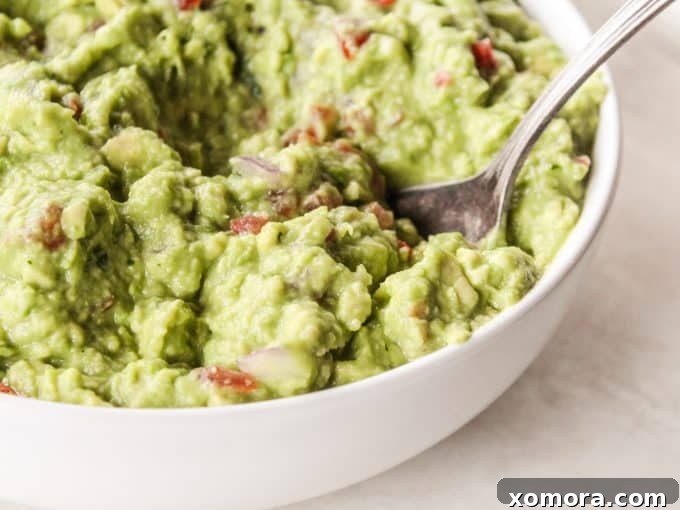 A close-up of chunky, green homemade guacamole with visible pieces of tomato and onion.