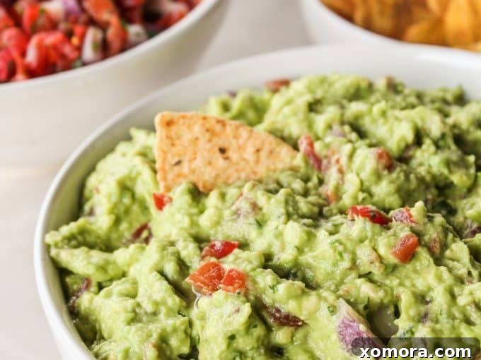 A bowl of homemade guacamole served with an array of colorful raw vegetables like carrots, cucumbers, and broccoli.